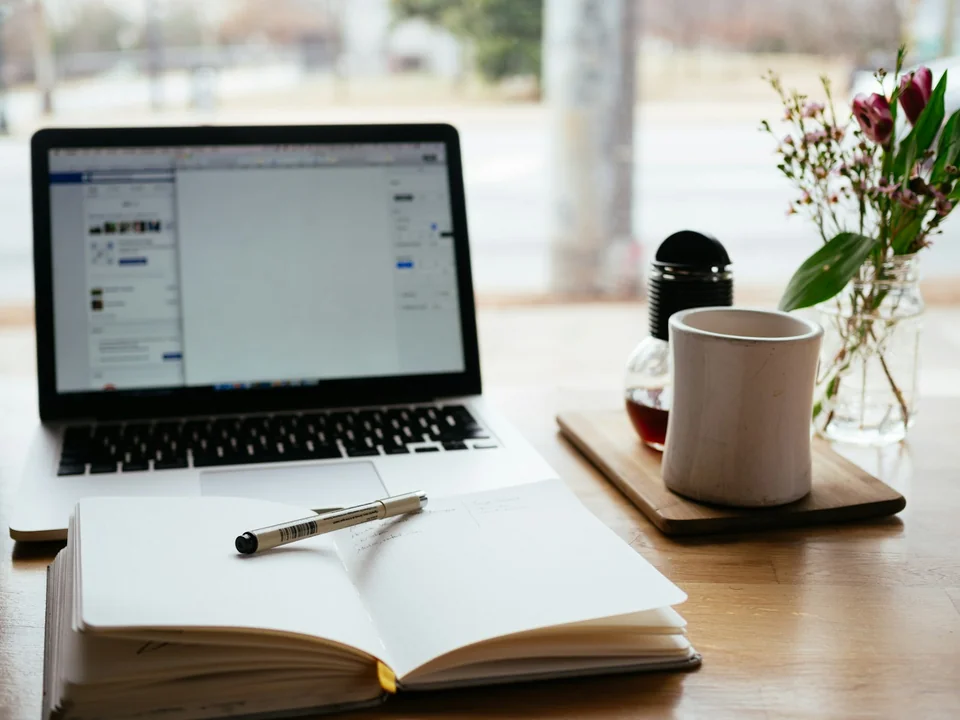 Laptop abierta junto a una libreta, café y material de trabajo.