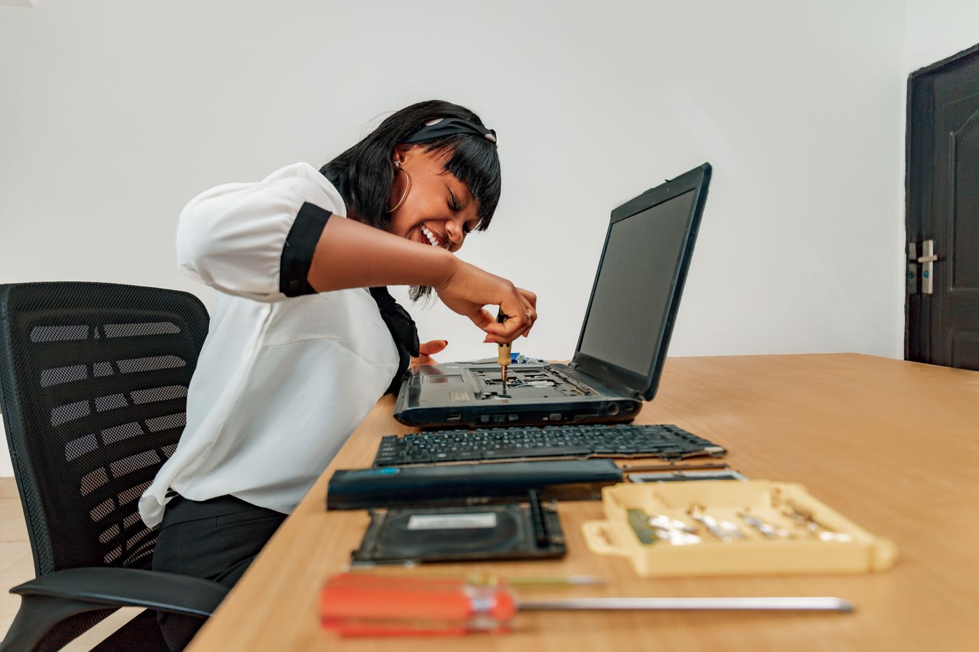 Técnica reparando una laptop abierta con herramientas en su mesa de trabajo.